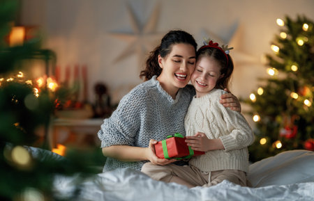 Merry Christmas and Happy Holidays. Cheerful mom and her cute daughter girl exchanging gifts. Parent and little child having fun near tree indoors. Loving family with presents in room.の写真素材