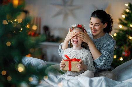 Merry Christmas and Happy Holidays. Cheerful mom and her cute daughter girl exchanging gifts. Parent and little child having fun near tree indoors. Loving family with presents in room.の写真素材