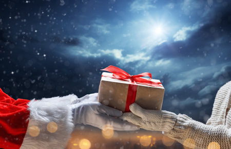 Merry Christmas and Happy Holidays. Hands of Santa Claus giving a x-mas gift to child.の写真素材