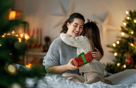 Merry Christmas and Happy Holidays. Cheerful mom and her cute daughter girl exchanging gifts. Parent and little child having fun near tree indoors. Loving family with presents in room.の写真素材