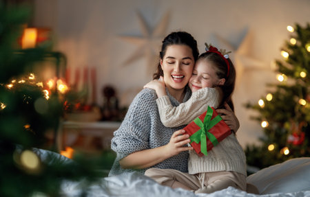 Merry Christmas and Happy Holidays. Cheerful mom and her cute daughter girl exchanging gifts. Parent and little child having fun near tree indoors. Loving family with presents in room.の写真素材