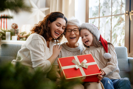 Merry Christmas and Happy Holidays. Cheerful kid presenting gifts to mom and granny. Parents and little child having fun near tree indoors. Loving family with presents in room.の写真素材