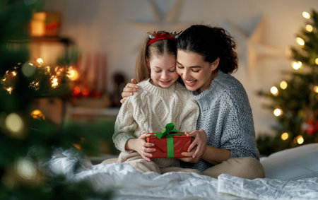 Merry Christmas and Happy Holidays. Cheerful mom and her cute daughter girl exchanging gifts. Parent and little child having fun near tree indoors. Loving family with presents in room.の写真素材