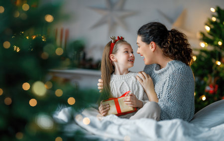 Merry Christmas and Happy Holidays. Cheerful mom and her cute daughter girl exchanging gifts. Parent and little child having fun near tree indoors. Loving family with presents in room.の写真素材