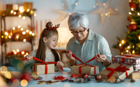 Happy Holidays. Cheerful grandmother and her cute granddaughter girl preparing for Christmas. People wrapping gifts, decorating home. Loving family with presents in room.の写真素材