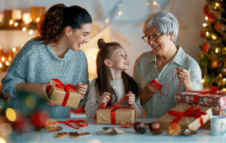 Happy Holidays. Cheerful grandmother, mother and cute daughter girl preparing for Christmas. People wrapping gifts, decorating home. Loving family with presents in room.の写真素材