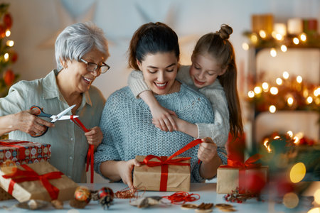 Happy Holidays. Cheerful grandmother, mother and cute daughter girl preparing for Christmas. People wrapping gifts, decorating home. Loving family with presents in room.の写真素材