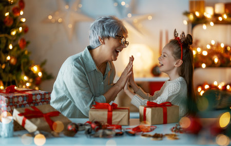 Happy Holidays. Cheerful grandmother and her cute granddaughter girl preparing for Christmas. People wrapping gifts, decorating home. Loving family with presents in room.の写真素材