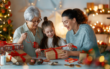 Happy Holidays. Cheerful grandmother, mother and cute daughter girl preparing for Christmas. People wrapping gifts, decorating home. Loving family with presents in room.の写真素材