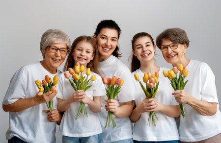 Happy women's day! Children daughters are congratulating mom and grandmothers giving them flowers tulips. Grannys, mom and girls smiling on light grey background. Family holiday and togetherness.の写真素材