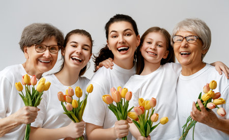 Happy women's day! Children daughters are congratulating mom and grandmothers giving them flowers tulips. Grannys, mom and girls smiling on light grey background. Family holiday and togetherness.の写真素材