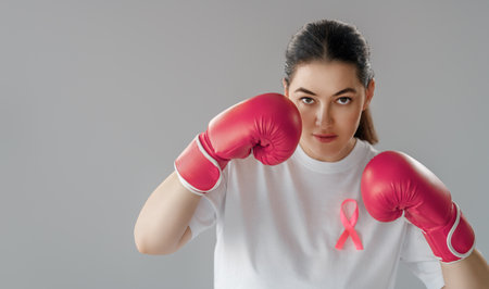 Woman in boxing gloves with a pink ribbon as a symbol of the fight against cancer. Increasing the level of knowledge about people who have overcome tumor diseases.の写真素材