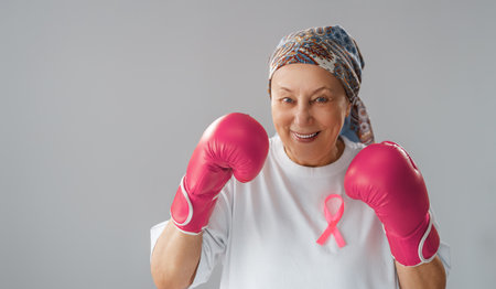 Woman in boxing gloves with a pink ribbon as a symbol of the fight against cancer. Increasing the level of knowledge about people who have overcome tumor diseases.の写真素材