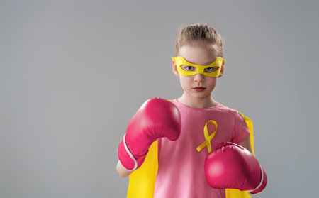 Child in boxing gloves with a yellow ribbon as a symbol of the fight against cancer. Increasing the level of knowledge about kids who have overcome tumor diseases.の写真素材