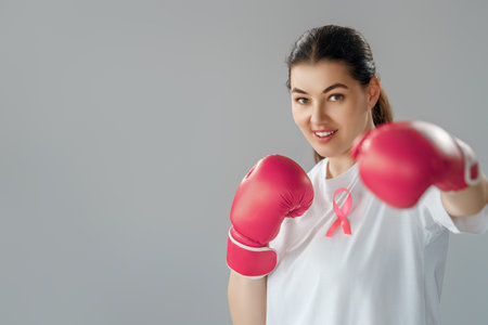 Woman in boxing gloves with a pink ribbon as a symbol of the fight against cancer. Increasing the level of knowledge about people who have overcome tumor diseases.の写真素材