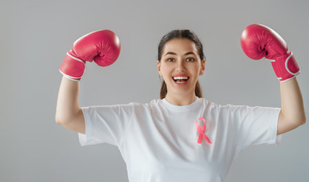 Woman in boxing gloves with a pink ribbon as a symbol of the fight against cancer. Increasing the level of knowledge about people who have overcome tumor diseases.の写真素材