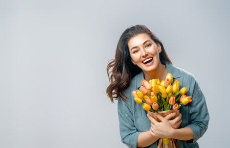 Beautiful young woman with yellow flowers in hands on grey wall background.の写真素材