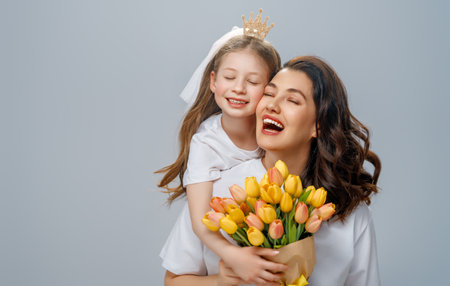 Happy women's day. Child is congratulating mom and giving her yellow flowers. Mum and girl smiling on light grey background. Family holiday and togetherness.の写真素材