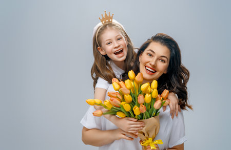 Happy women's day. Child is congratulating mom and giving her yellow flowers. Mum and girl smiling on light grey background. Family holiday and togetherness.の写真素材