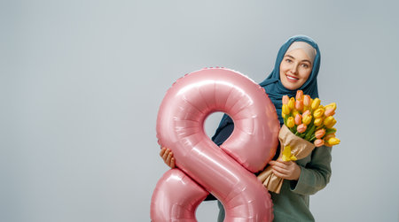 Beautiful young woman with yellow flowers and a balloon in the shape of an eight on gray wall background.の写真素材
