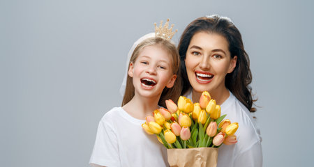 Happy women's day. Child is congratulating mom and giving her yellow flowers. Mum and girl smiling on light grey background. Family holiday and togetherness.の写真素材
