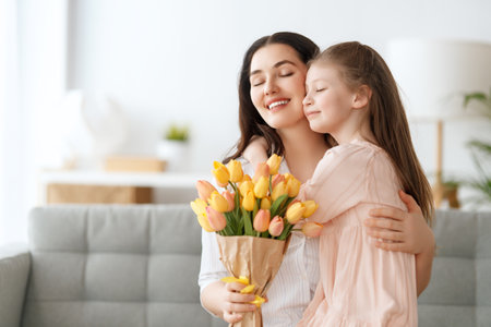 Happy mother's day. Child daughter is congratulating mom and giving her flowers. Mum and girl smiling and hugging. Family holiday and togetherness.の写真素材