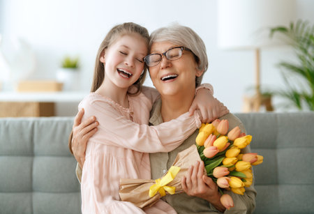 Happy mother's day. Child is congratulating granny giving her flowers. Grandma and girl smiling and hugging. Family holiday and togetherness.の写真素材
