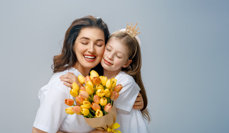 Happy women's day. Child is congratulating mom and giving her yellow flowers. Mum and girl smiling on light grey background. Family holiday and togetherness.の写真素材