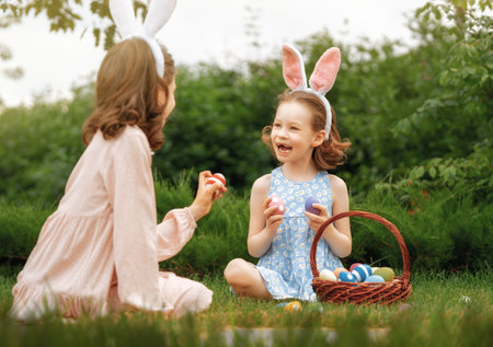 Beautiful children with painting eggs outdoors. Happy family celebrating Easter in nature. Cute little girls are wearing bunny ears.の写真素材