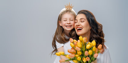 Happy women's day. Child is congratulating mom and giving her yellow flowers. Mum and girl smiling on light grey background. Family holiday and togetherness.の写真素材