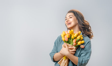 Beautiful young woman with yellow flowers in hands on grey wall background.の写真素材