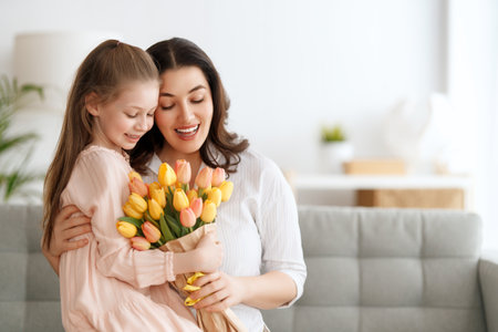 Happy mother's day. Child daughter is congratulating mom and giving her flowers. Mum and girl smiling and hugging. Family holiday and togetherness.の写真素材