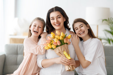 Happy mother's day. Children daughters are congratulating mom and giving her flowers. Mum and girls smiling and hugging. Family holiday and togetherness.の写真素材