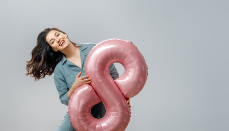 Beautiful young woman with a balloon in the shape of an eight on gray wall background.の写真素材