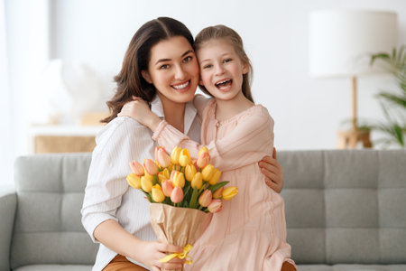 Happy mother's day. Child daughter is congratulating mom and giving her flowers. Mum and girl smiling and hugging. Family holiday and togetherness.の写真素材