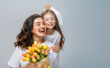Happy women's day. Child is congratulating mom and giving her yellow flowers. Mum and girl smiling on light grey background. Family holiday and togetherness.の写真素材