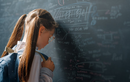 Back to school. Unhappy kid indoors. Girl is learning in class on background of blackboard.の写真素材