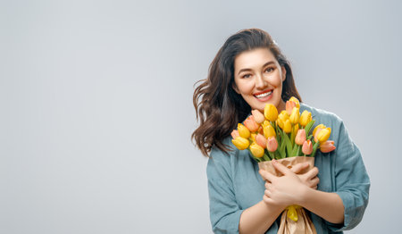Beautiful young woman with yellow flowers in hands on grey wall background.の写真素材