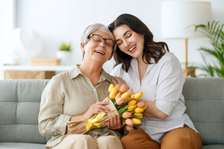 Beautiful young woman and her mother with flowers tulips in hands at home.の写真素材