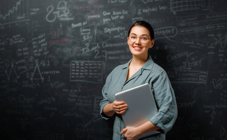 Back to school. Happy teacher indoors. Woman is standing in class on background of blackboard.の写真素材