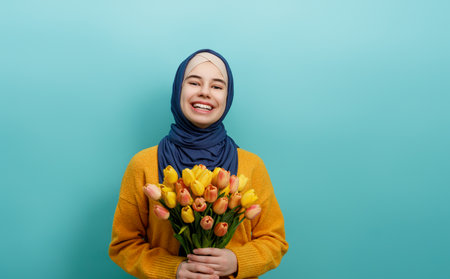 Beautiful young girl with yellow flowers in hands on teal wall background.の写真素材