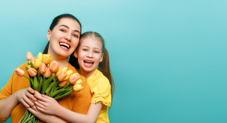 Happy women's day. Child is congratulating mom and giving her yellow flowers. Mum and girl smiling on teal background. Family holiday and togetherness.の写真素材