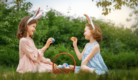 Beautiful children with painting eggs outdoors. Happy family celebrating Easter in nature. Cute little girls are wearing bunny ears.の写真素材