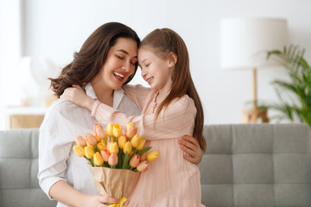Happy mother's day. Child daughter is congratulating mom and giving her flowers. Mum and girl smiling and hugging. Family holiday and togetherness.の写真素材