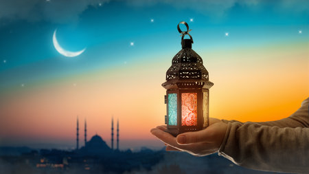 Ornamental Arabic lantern with burning candle glowing at night mosque background. Festive greeting card, invitation for Muslim holy month Ramadan Kareem.の写真素材