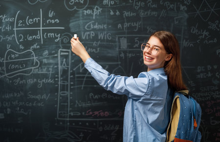 Back to school. Happy cute industrious teenager indoors. Girl is learning in class on background of blackboard.の写真素材