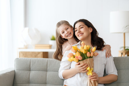 Happy mother's day. Child daughter is congratulating mom and giving her flowers. Mum and girl smiling and hugging. Family holiday and togetherness.の写真素材