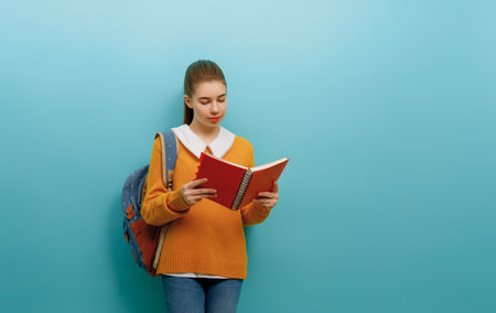 Back to school and happy time. Cute industrious teenager on color paper wall background. Girl with backpack. Teen ready to study.の写真素材