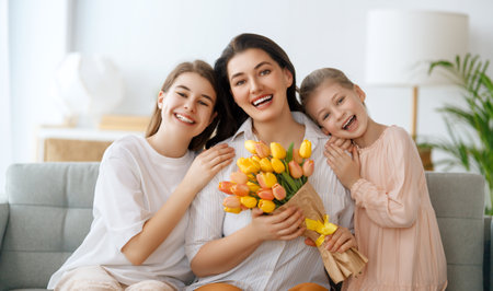Happy mother's day. Children daughters are congratulating mom and giving her flowers. Mum and girls smiling and hugging. Family holiday and togetherness.の写真素材