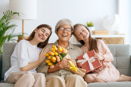 Happy mother's day! Children daughters are congratulating grandmother and giving her flowers. Granny and girls smiling and hugging. Family holiday and togetherness.の写真素材